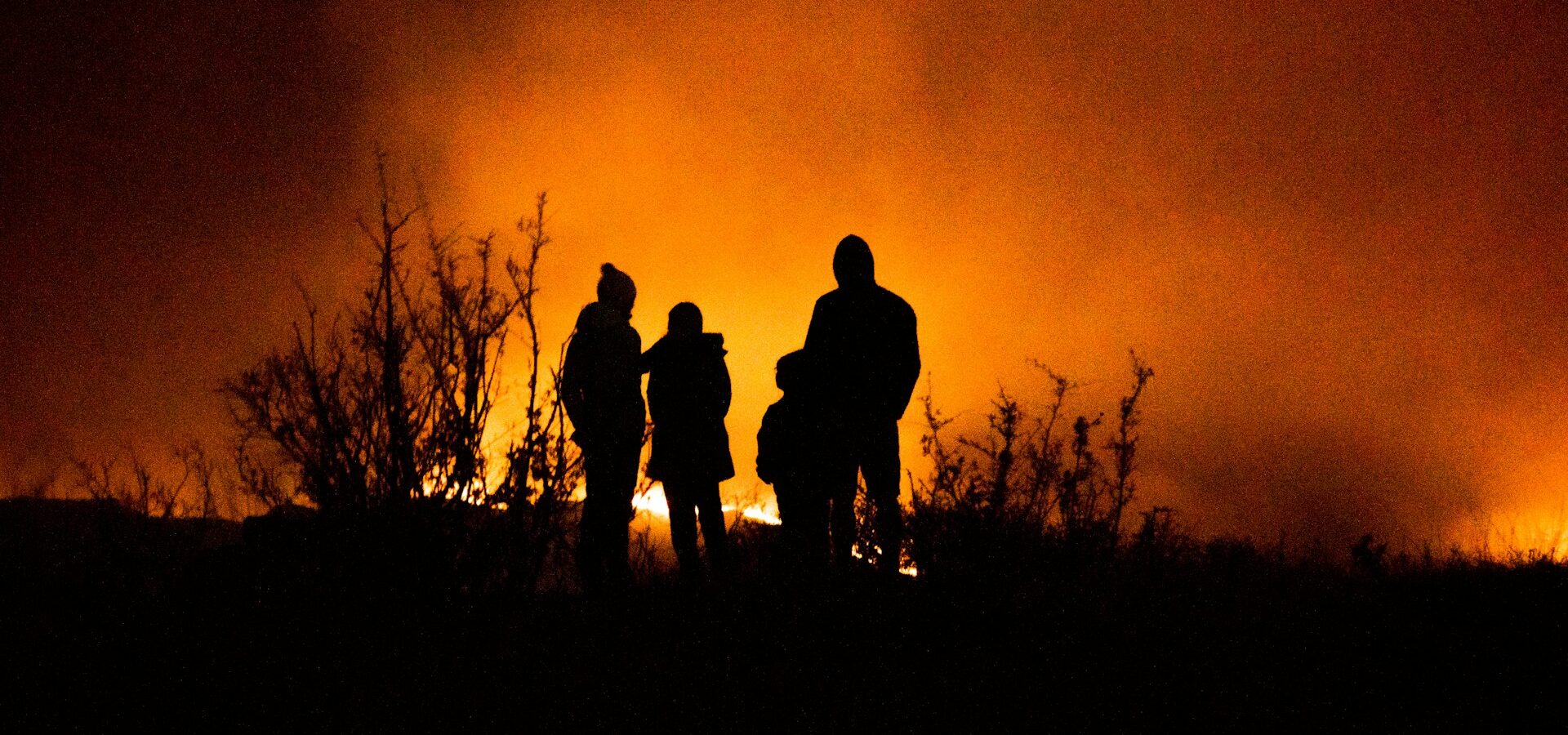 Family on a hill looking at a fire, silhouetted by the flames