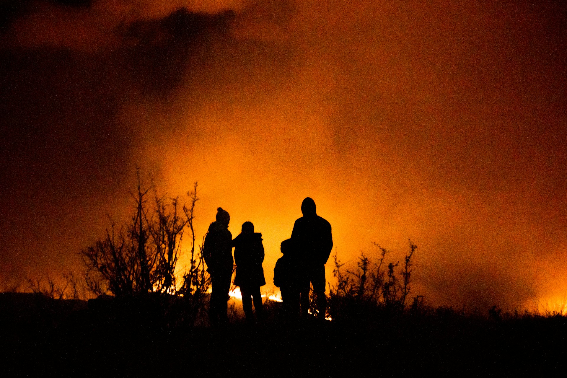 Family on a hill looking at a fire, silhouetted by the flames
