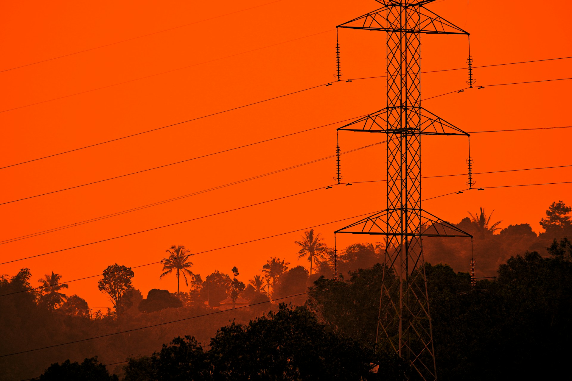 Electrical transmission tower in the forested hills with the sky red from a wildfire
