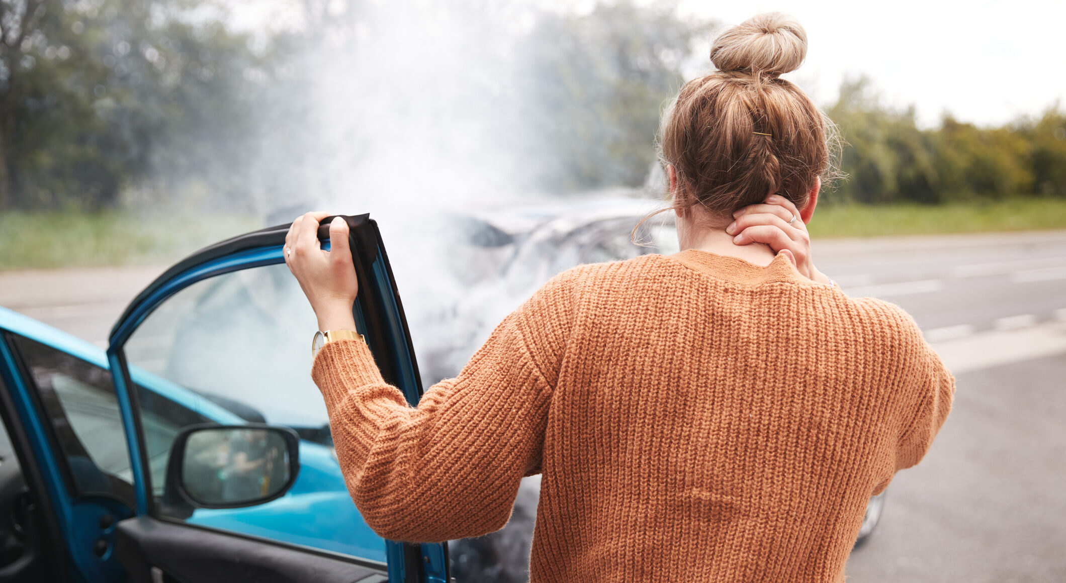 Rear View Of Female Motorist With Head Injury Getting Out Of Car After Crash
