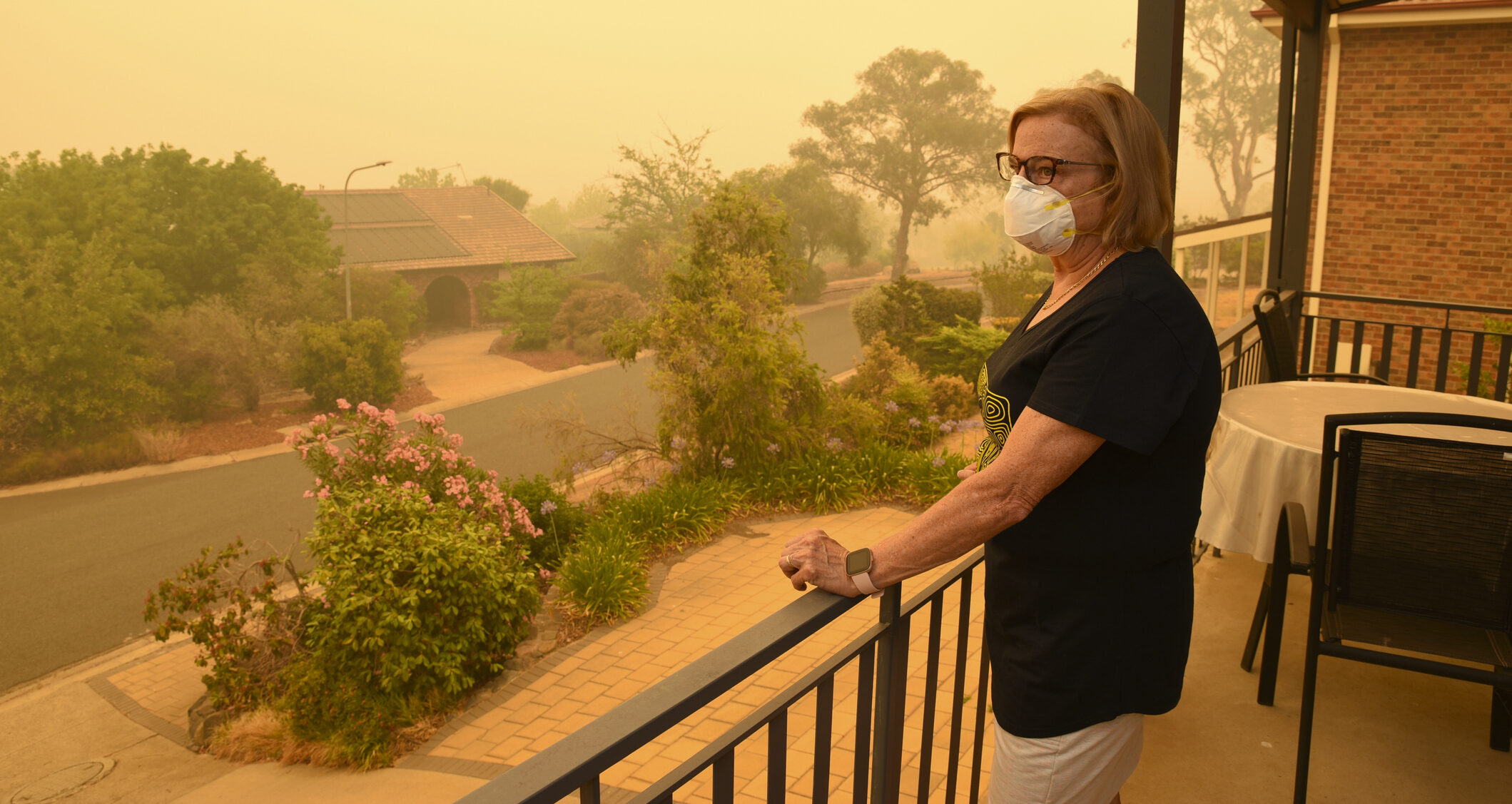 A woman, on a balcony, wears a face mask to protect herself against very dangerous level of air pollution. A thick yellow fog coming from the nearby forest fires