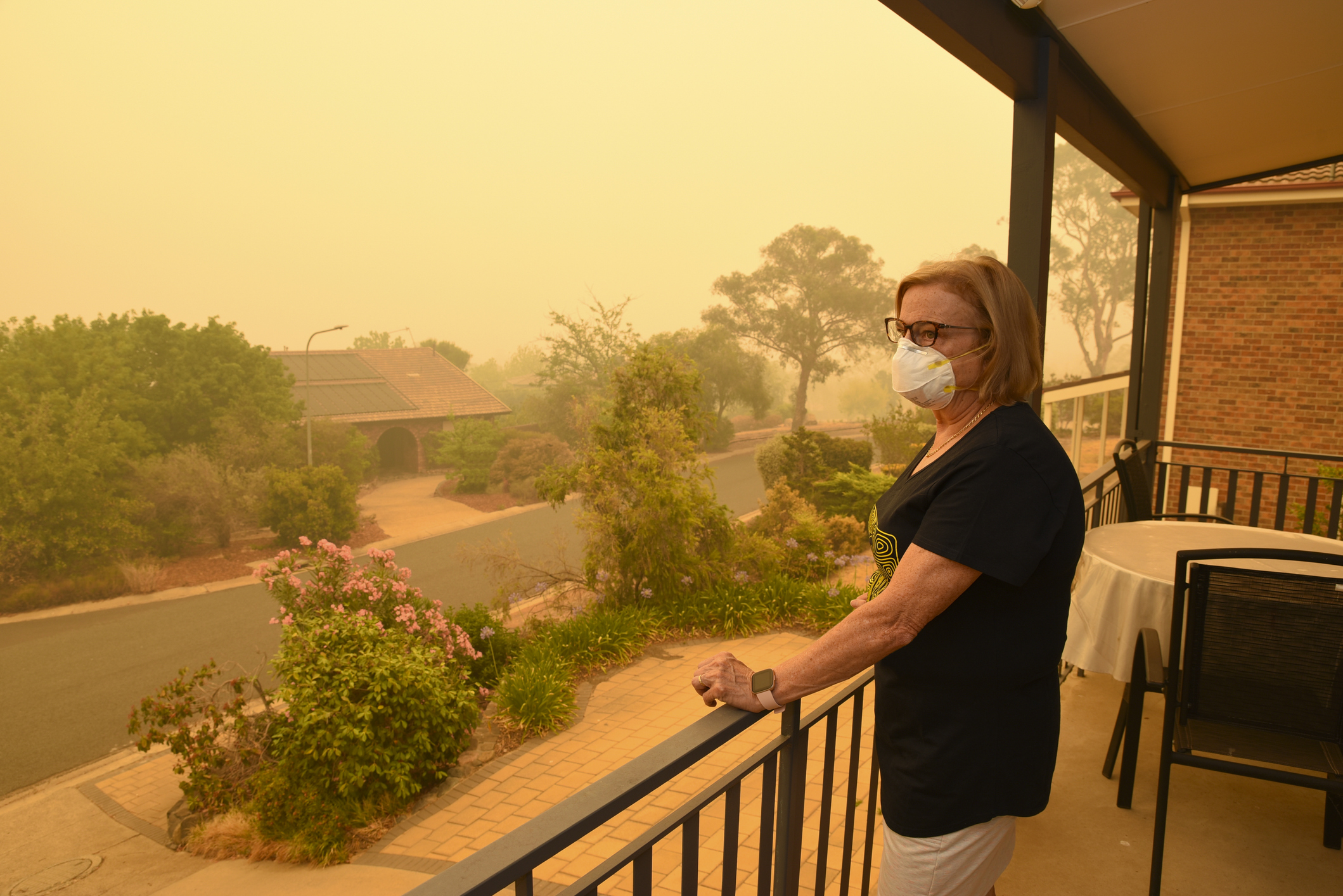 A woman, on a balcony, wears a face mask to protect herself against very dangerous level of air pollution. A thick yellow fog coming from the nearby forest fires