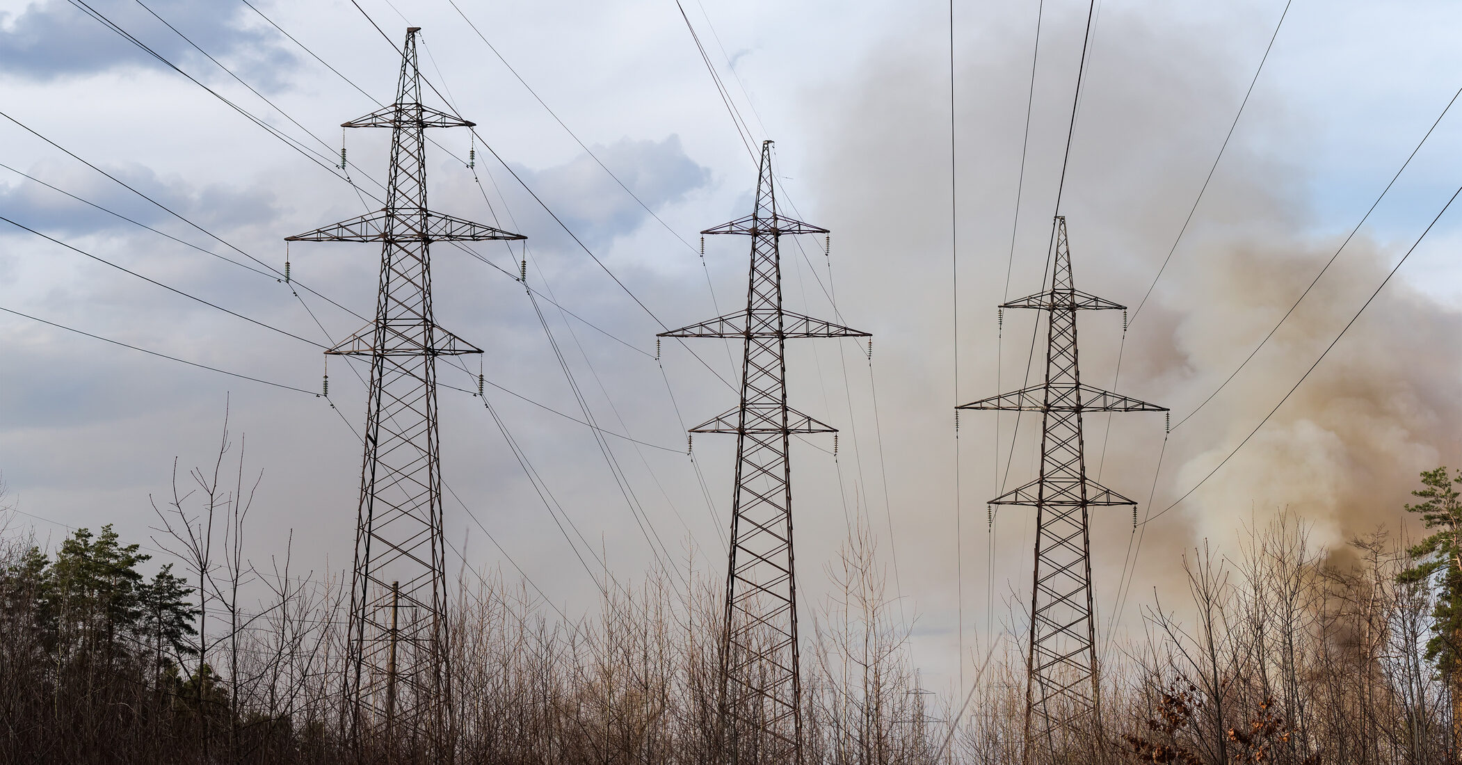 Overhead power lines over the forest clearing against the sky is covered with smoke from the fire