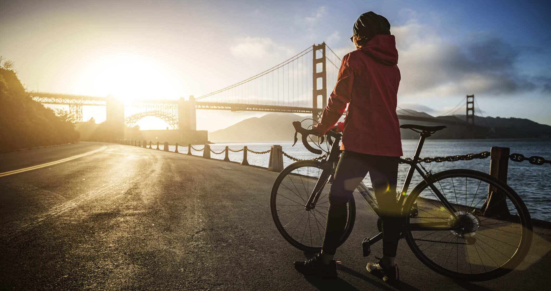 cyclist with bike watching sun set behind the golden gate bridge